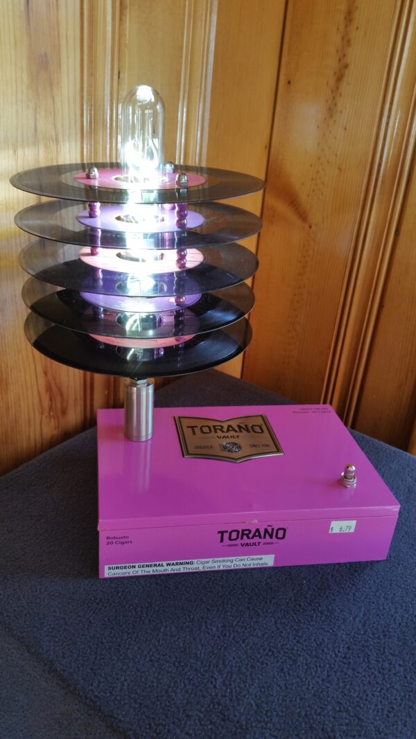 Front view of Hot Pink Torano Cigar Box Lamp Topped with a stack of purple & pink labled 45 records which cause the lamp to have a subtle pink glow when lit.