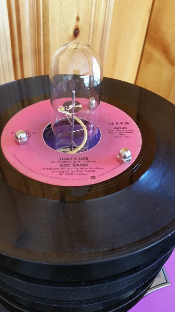 Top record view of Hot Pink Torano Cigar Box Lamp Topped with a stack of purple & pink labled 45 records which cause the lamp to have a subtle pink glow when lit.