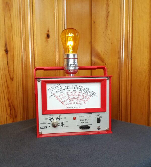 Made for the motorhead in your life. A red automobile diagnostic meter made into a lamp with a yellow light bulb on top.