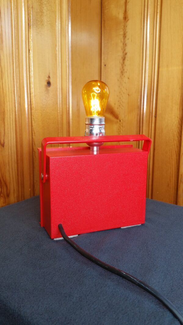 Made for the motorhead in your life. The back of of a red automobile diagnostic meter made into a lamp with a yellow light bulb on top.