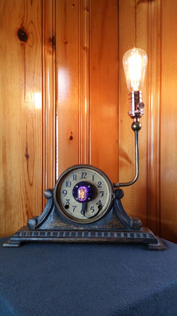 A mantle clock with Nixie tube in the middle of the clock face and a upturned arm coming out of the side topped by copper socket and an Edison-style light bulb.