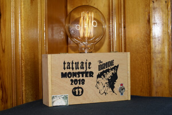A cigar box lamp with Monster 2018 and Bride of Frankenstein graphics on the front. Topped with a round Edison Style bulb. Monster Lamp Horror Fan Favorite