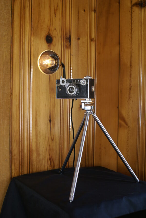 A vintage black and silver Argus camera mounted to a vintage chrome tripod. The camera has a light socket that mimics a flash.