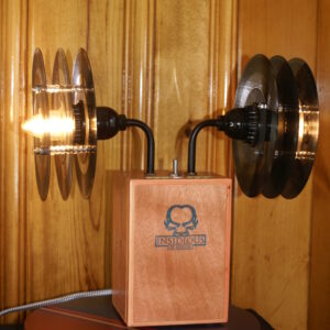 A cigar box lamp with two 90 degree bent elbows that project to each side and have two light sockets pointing in opposite directions. The light bulbs are shaded with two shades that have been fabricated from vintage 45 rpm records.