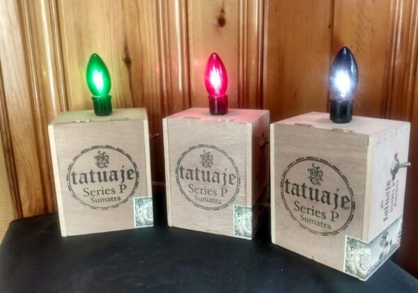 A cigar box lamp with small fleur di lis and the word Tatauje on the front. The lamp has a large colored christmas style bulb on top.